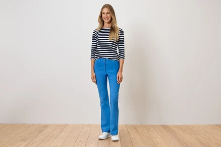 Frau steht und trägt blaue Hosen, ein gestreiftes T-Shirt und weiße Schuhe.