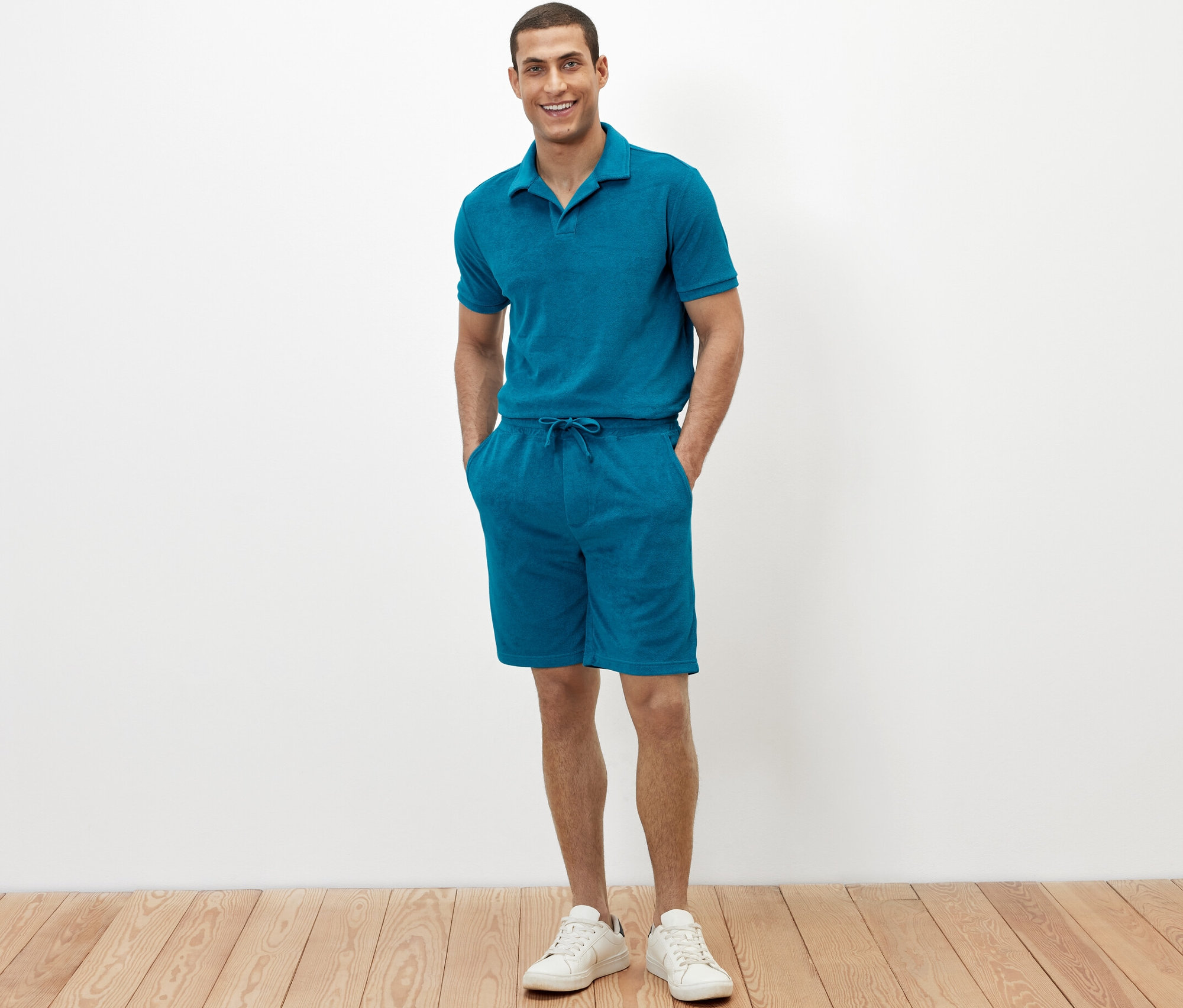 Mann steht mit den Händen in den Taschen seiner petrolfarbenen Frottee-Shorts.