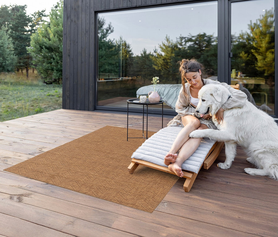 Frau sitzt auf einer Liege auf einer Holzterrasse und umarmt einen großen weißen Hund. Auf der Terrasse liegt ein brauner Teppich »Roy«, Lines, ca. 120 x 170 cm.