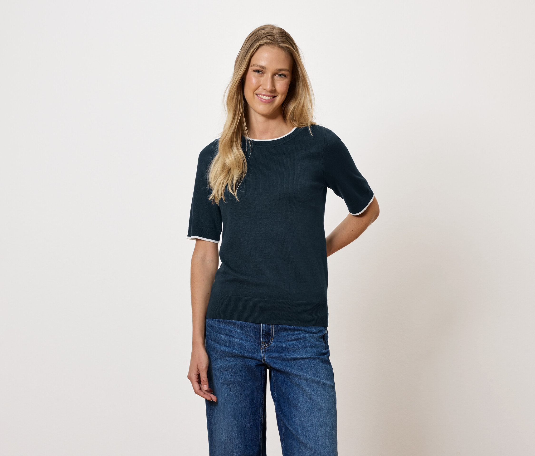 Frau mit blonden Haaren trägt ein dunkelblaues Kurzarm-Top und Jeans.