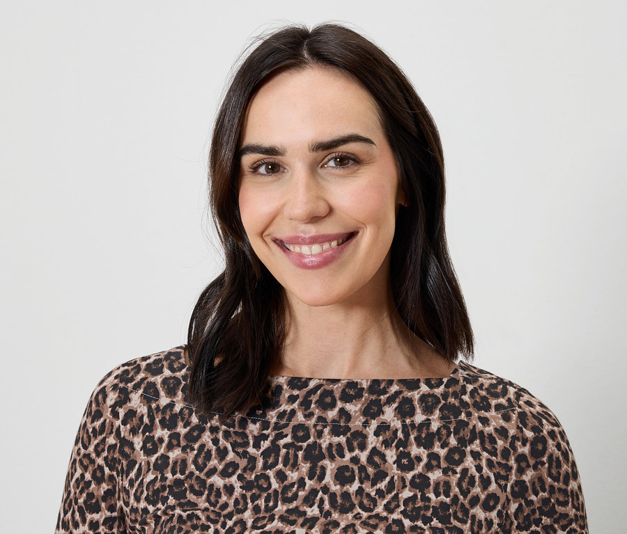 Porträt einer lächelnden Frau mit braunen Haaren in einem Oberteil mit Leopardenmuster.