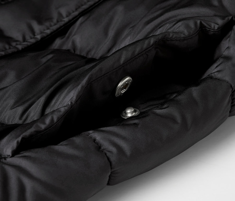 Detailaufnahme einer schwarzen Steppjacke mit offener Tasche und zwei silbernen Druckknöpfen.
