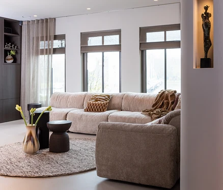 Wohnzimmer mit beigem Modulsofa, braunem Kissen und brauner Decke auf dem runden Woood Teppich Efia.