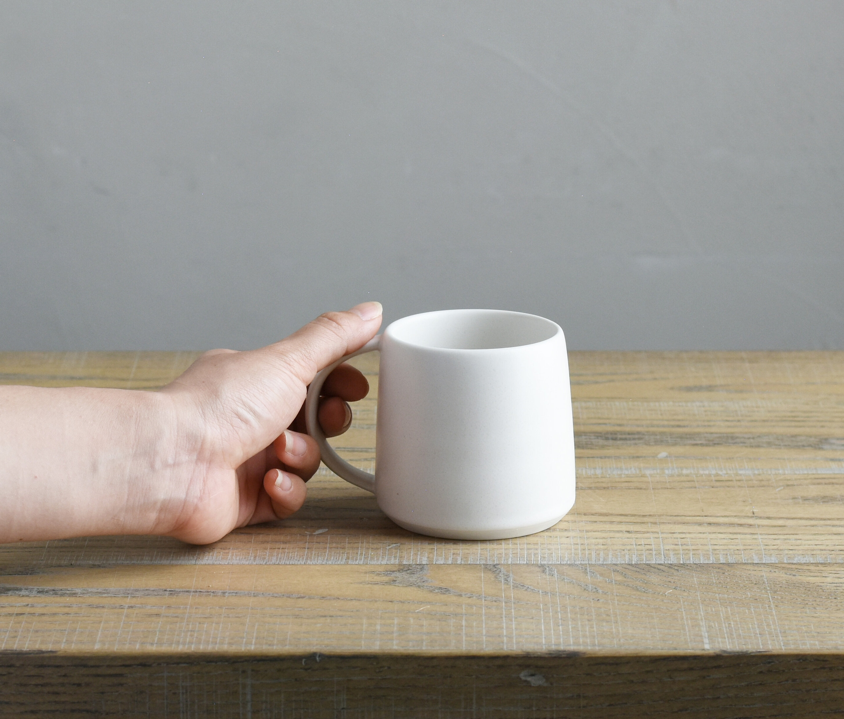 Eine Hand hält eine weiße Tasse auf einem Holztisch.