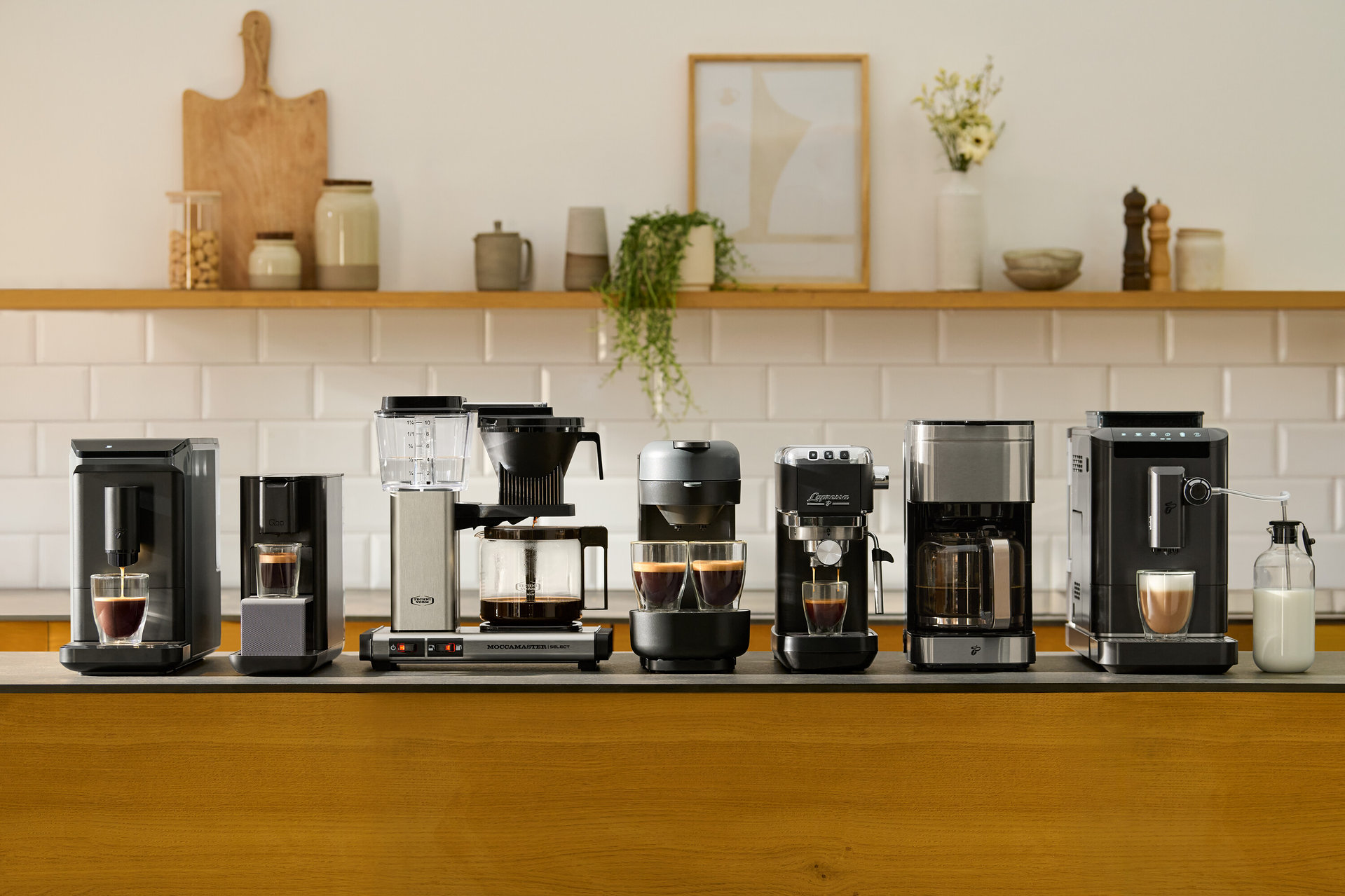Verschiedene Kaffeemaschinen stehen auf einer Küchentheke vor einer weißen Fliesenkulisse.