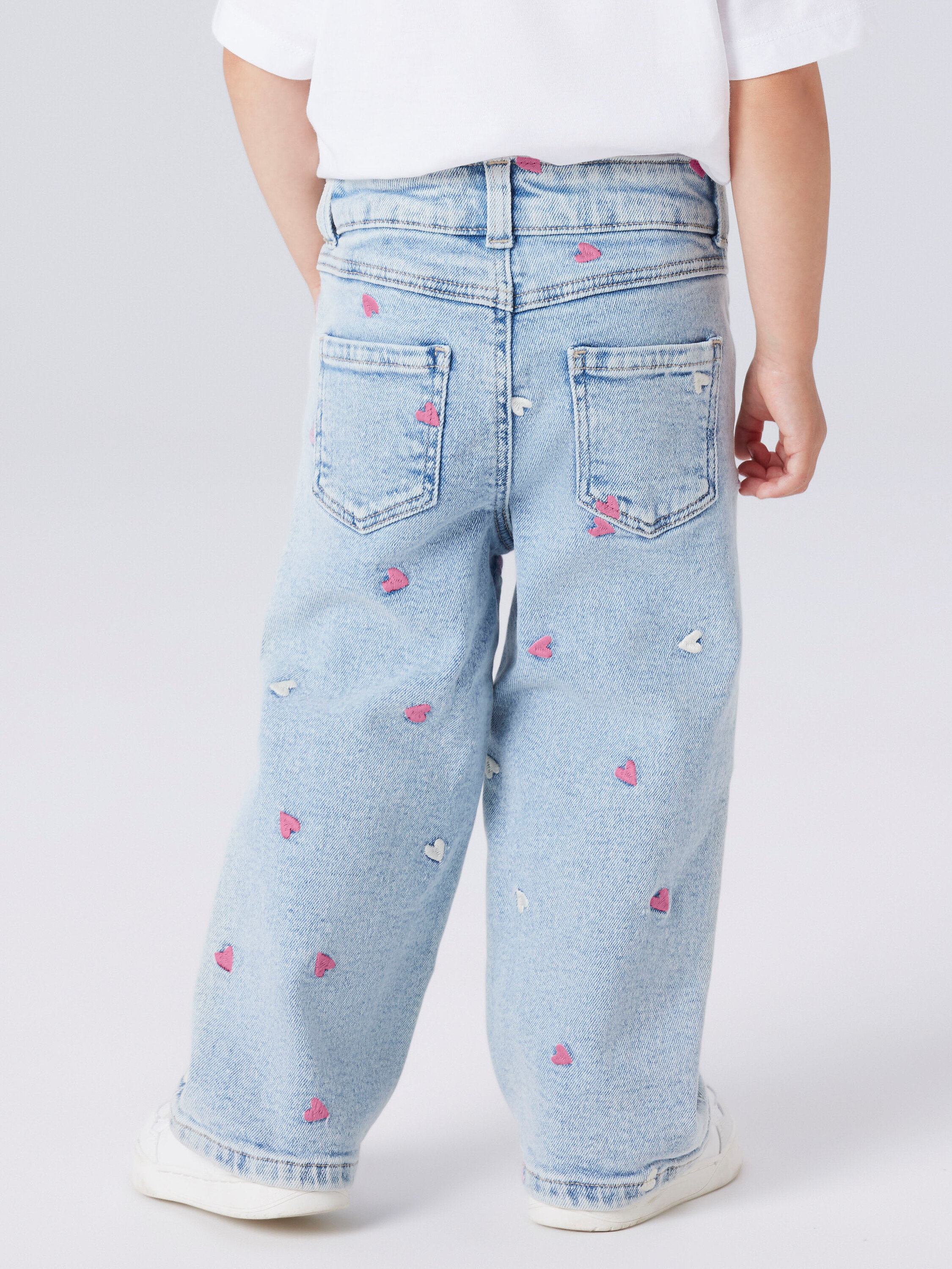 Rückansicht eines Kindes mit hellblauen Jeans mit rosa und weißen Herzaufdrucken.