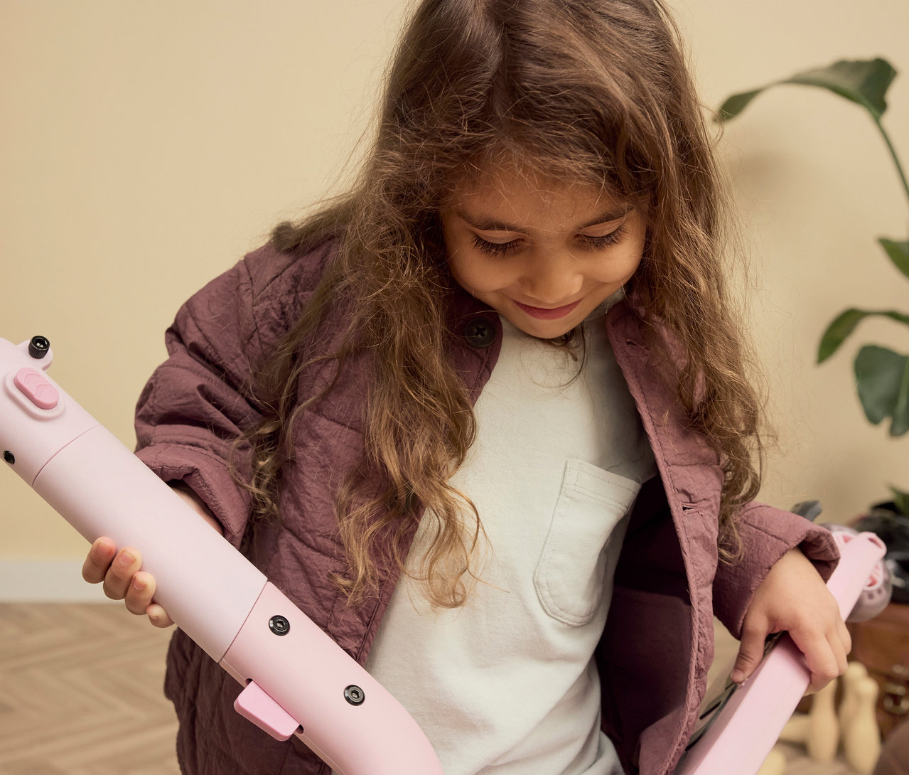 Mädchen mit braunen Haaren hält einen rosa PUKY Roller PUSH in den Händen und betrachtet ihn.