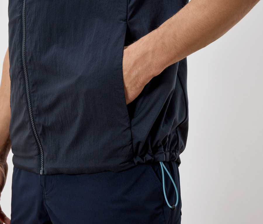 Nahaufnahme einer Person in marineblauer Weste und Hose, mit einer Hand in der Westentasche.