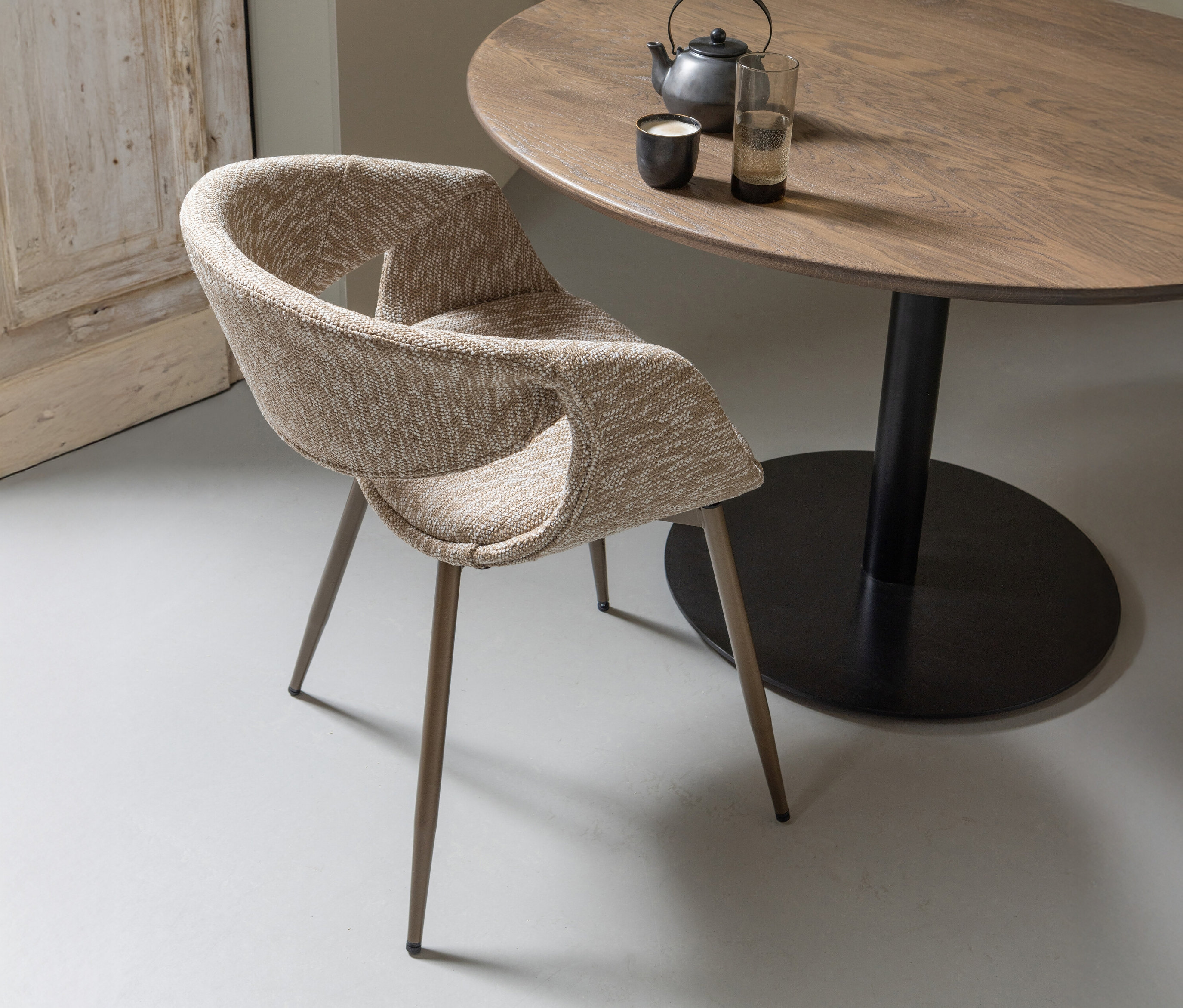 Ein kupfer-sandfarbener WOOOD Esszimmerstuhl »Yossi« mit Metallfuß steht neben einem runden Holztisch mit Teekanne und Gläsern.