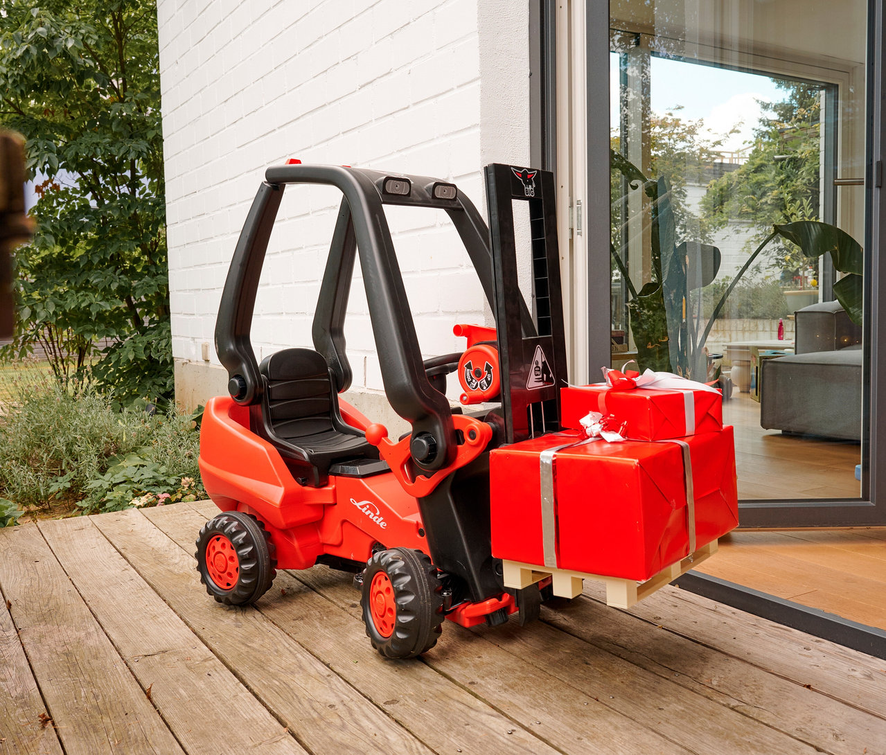 Der rote BIG Tretfahrzeug »Linde Gabelstapler« steht draußen und transportiert zwei rote Geschenke.