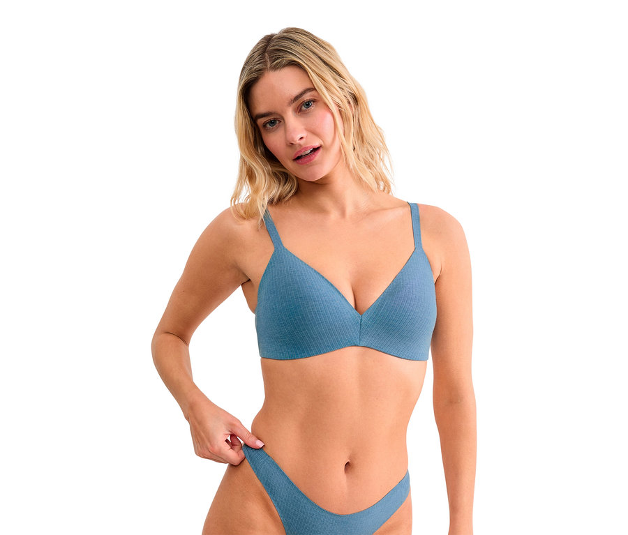 Blonde Frau in einem gerippten blauen BH und passendem Slip, die in die Kamera blickt und den Bund ihres Slips hält.