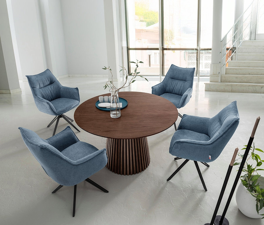Vier blaue, drehbare DeVries Diningsessel »Ginosa« um einen runden Holztisch in einem hellen Raum.