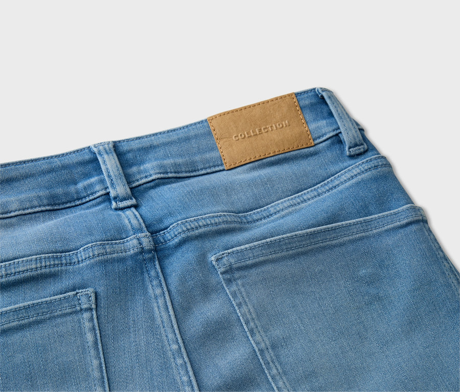 Detailansicht der Rückseite einer hellblauen Jeans mit braunem 'Collection'-Etikett.