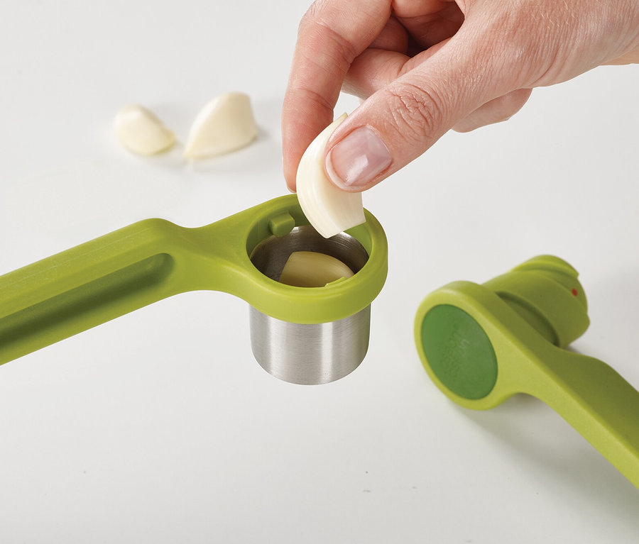 Eine Hand legt eine Knoblauchzehe in eine grüne Knoblauchpresse.