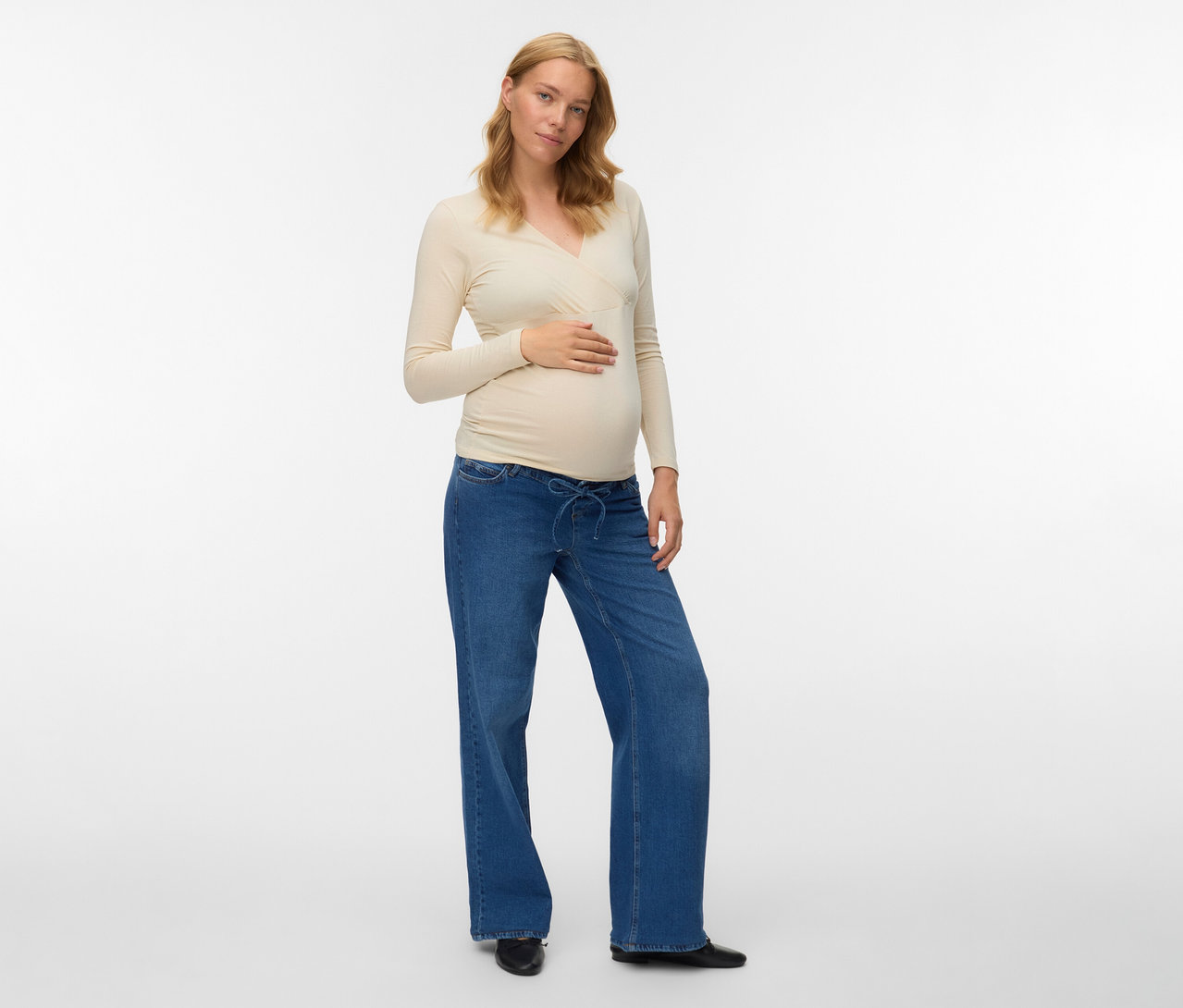 Schwangere trägt ein beigefarbenes MAMALICIOUS 2er Pack Top »MLKERRIE«, Jeans und Schuhe.
