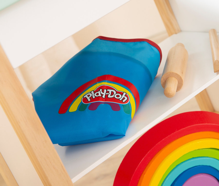 Auf einem Regal liegen eine blaue Play-Doh-Dose, ein Nudelholz und ein Holzregenbogen.