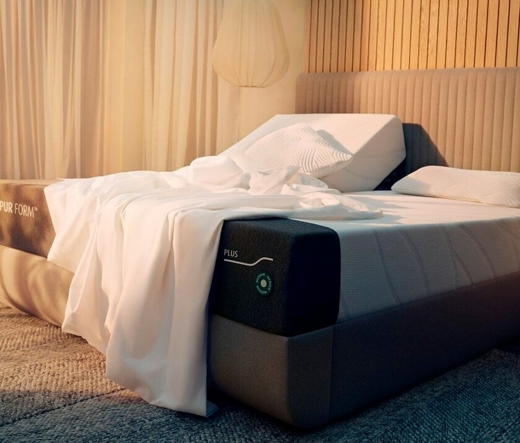 Eine Tempur Form Matratze mit weißer Bettwäsche, einem Keilkissen und einem Kopfkissen steht auf einem Bettgestell mit Kopfteil.