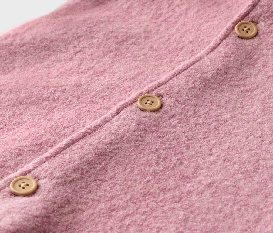 Nahaufnahme eines rosafarbenen Strickstoffes mit drei hellbraunen Knöpfen.