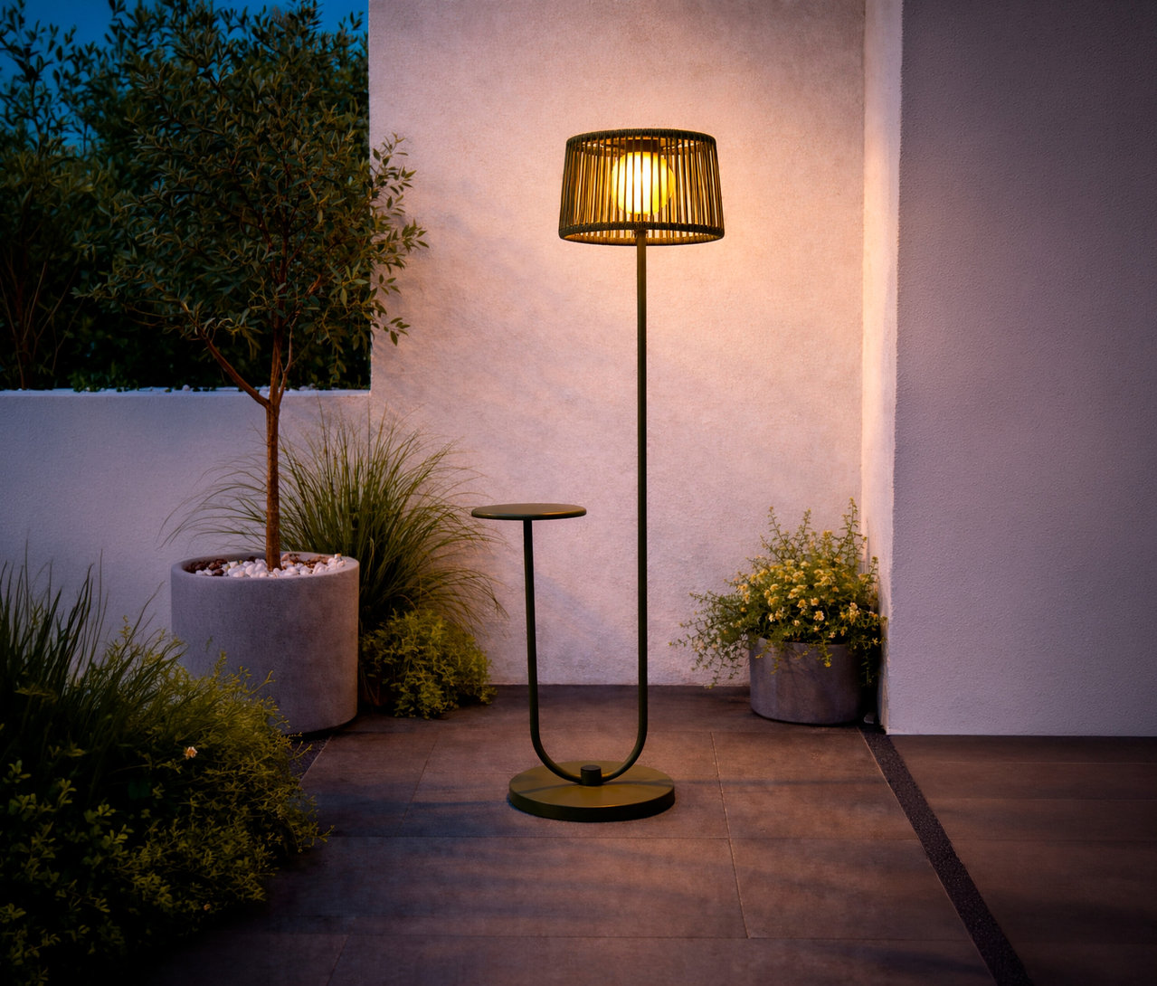 Grüne Leco Solar Stehleuchte mit integriertem Tisch steht auf einer Terrasse neben Pflanzen.