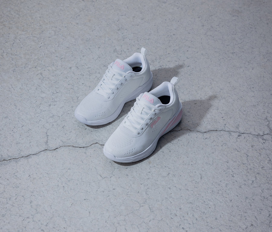 Zwei weiße Fila-Sneaker mit pinkfarbenem Logo liegen auf einem grauen Untergrund.