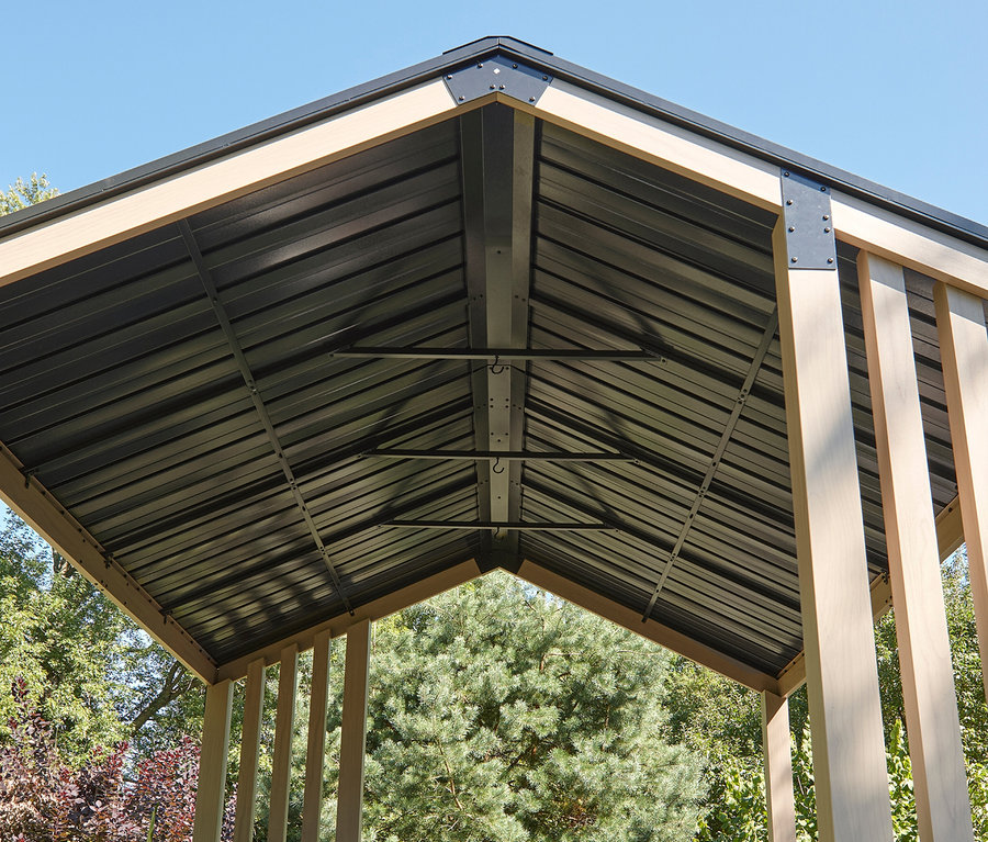 Ansicht des Metalldachs eines Pavillons mit hellbraunen Holzpfosten vor Bäumen.