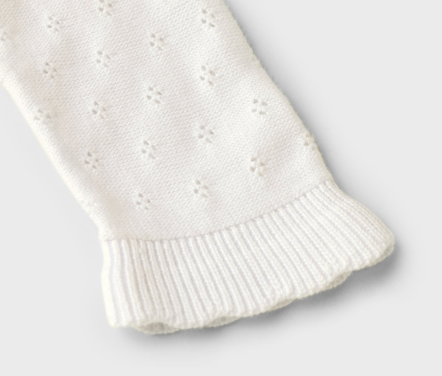 Ärmel eines weißen Strickpullovers mit Lochmuster und Rüschensaum, Nahaufnahme.