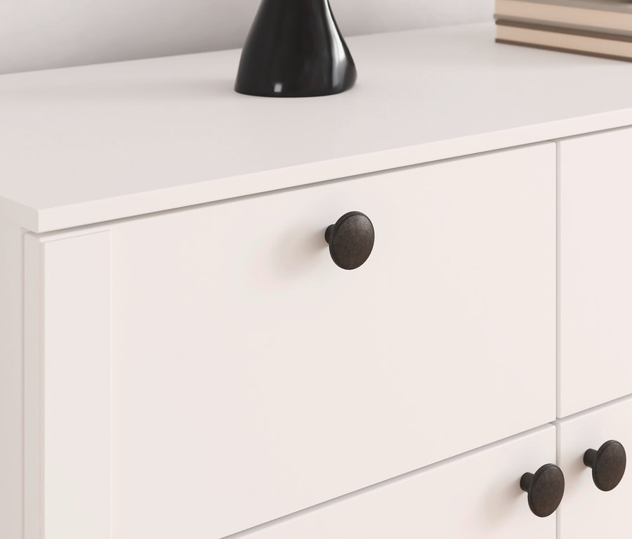 Nahaufnahme einer weißen Kommode mit Schubladen und dunklen Knöpfen, darauf eine schwarze Vase und Bücher.
