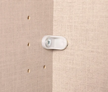 Nahaufnahme einer weißen Halterung mit Schraube an einer beigen Wand mit Löchern.