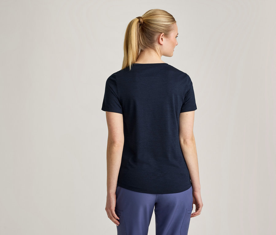 Frau von hinten gesehen, mit blonden Haaren im Pferdeschwanz, trägt ein dunkelblaues T-Shirt und hellblaue Hosen.