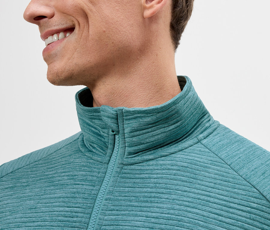 Nahaufnahme eines Mannes, der ein türkisfarbenes Fleece-Oberteil mit Reißverschluss trägt.