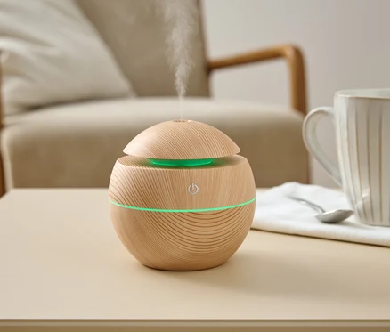 Ein hölzerner Luftbefeuchter mit grünem Licht steht auf einem Tisch neben einer Tasse und einem Löffel.