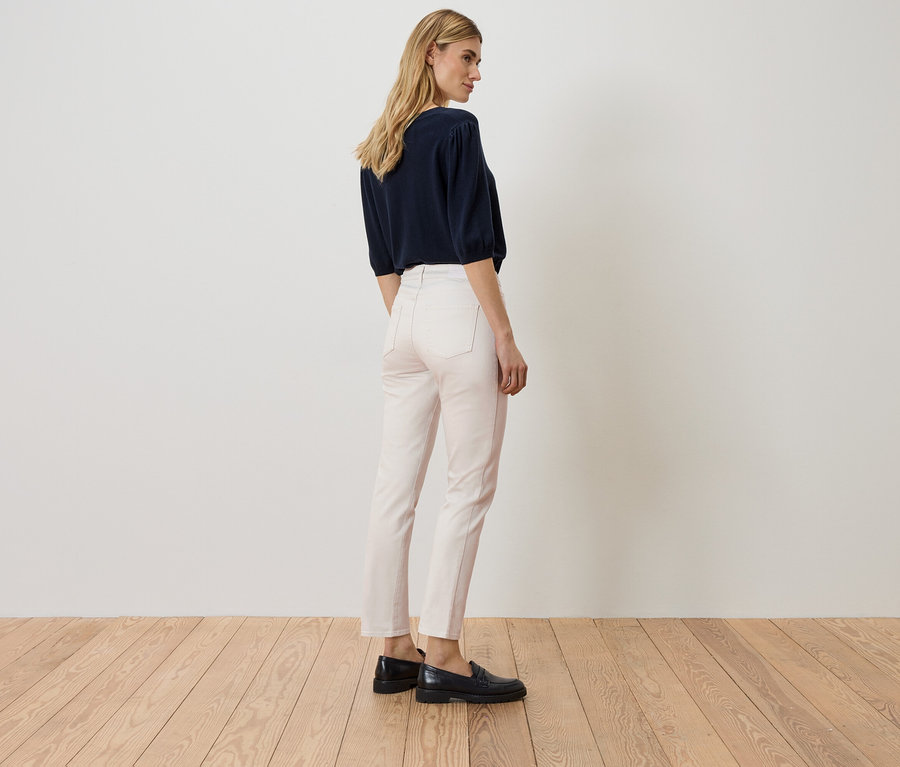 Frau steht mit dem Rücken zum Betrachter, trägt ein marineblaues Oberteil, rosafarbene Jeans und schwarze Schuhe.