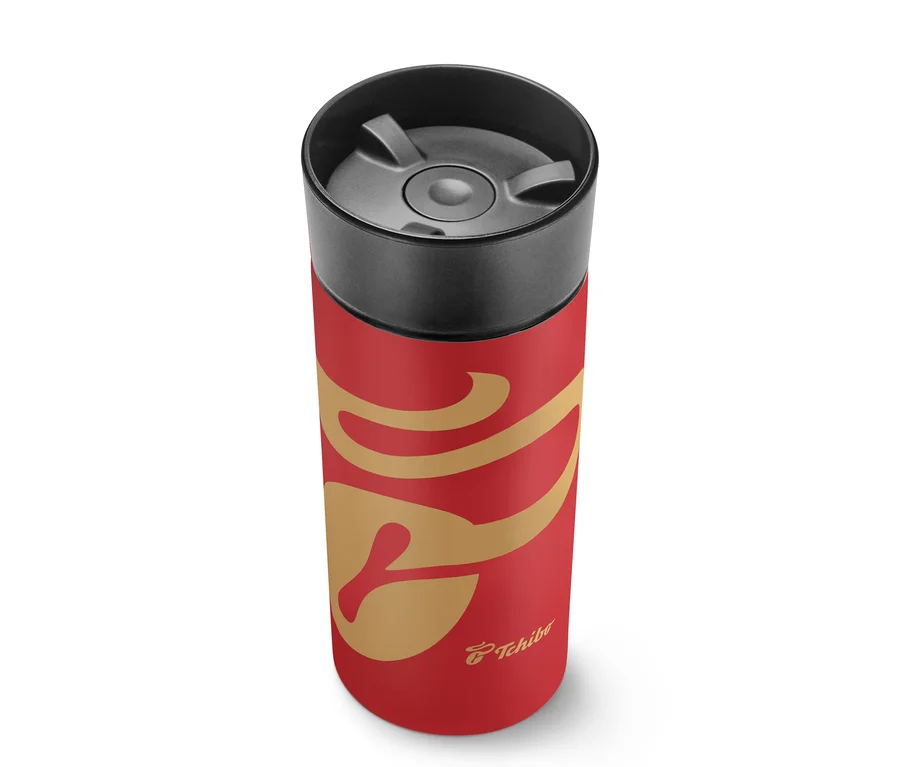 Rote Thermoskanne mit goldenem Schnörkelmuster und schwarzem Deckel, mit Tchibo-Logo.