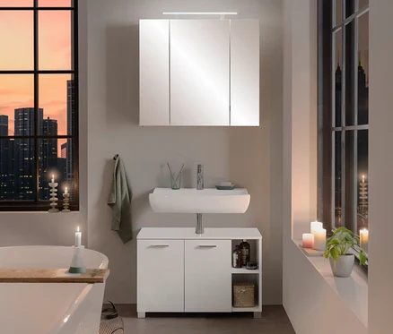 Modernes Badezimmer mit weißer Badewanne, einem Waschbecken mit Unterschrank und dem 80 cm breiten Spiegelschrank »Dorina« mit Licht. Kerzen und Stadtblick durch große Fenster schaffen eine gemütliche Atmosphäre.