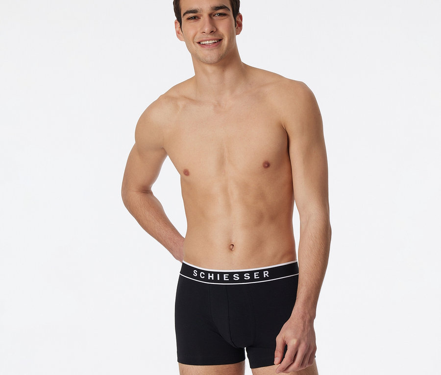 Lächelnder Mann in schwarzen SCHIESSER Shorts mit weißem Bund, Teil eines 3er-Packs.