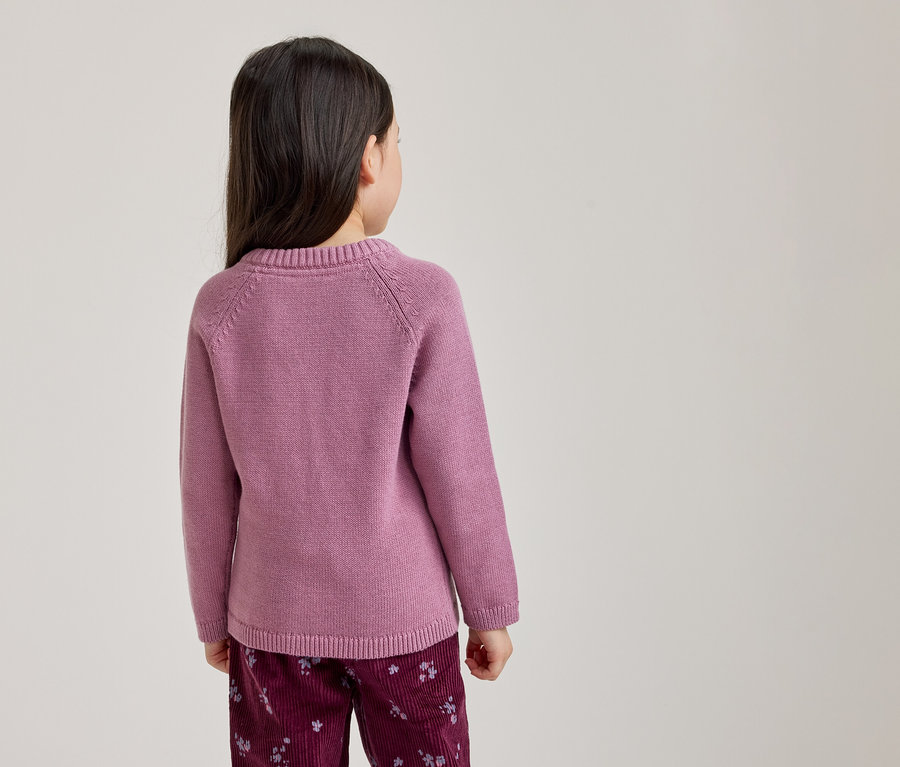 Ein junges Mädchen von hinten gesehen, das einen rosa Langarmpullover und dunkelrote Hosen mit hellem Blumenmuster trägt.