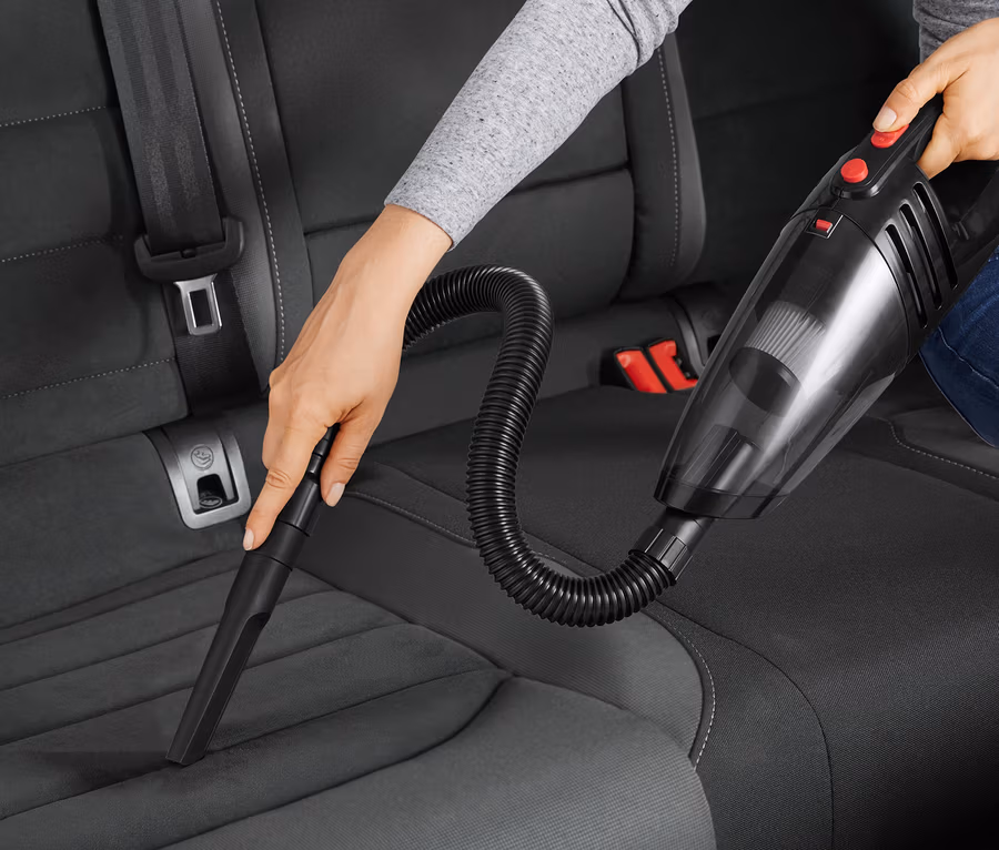 Frau saugt den Autositz mit einem Autostaubsauger.