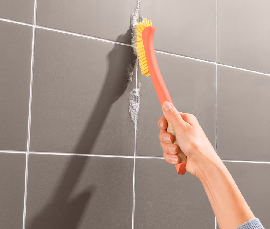 Eine Frau reinigt Fliesenfugen mit einer Fugenbürste.