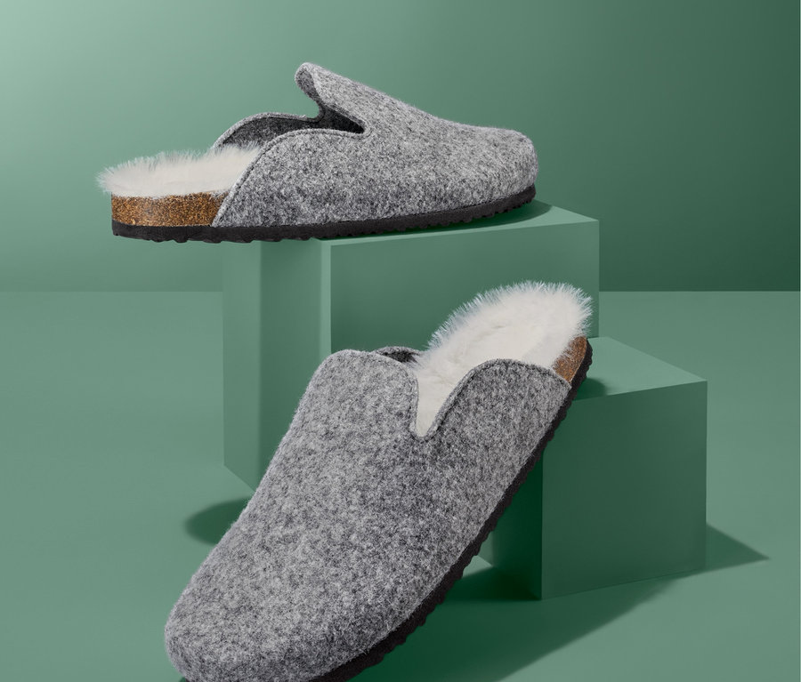 Zwei graue Hausschuhe auf grünen Sockeln.