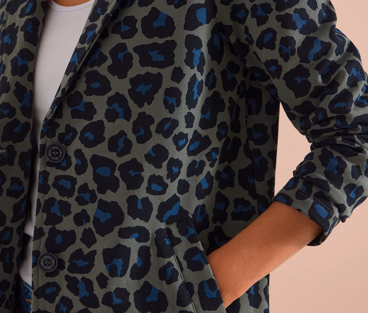 Person trägt einen CECIL Jerseyblazer mit grünem, schwarzem und blauem Leopardenmuster, die Hand in der Tasche.