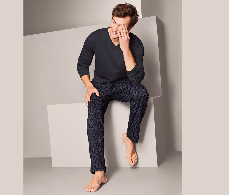 Mann sitzt und lacht, trägt einen Pyjama.