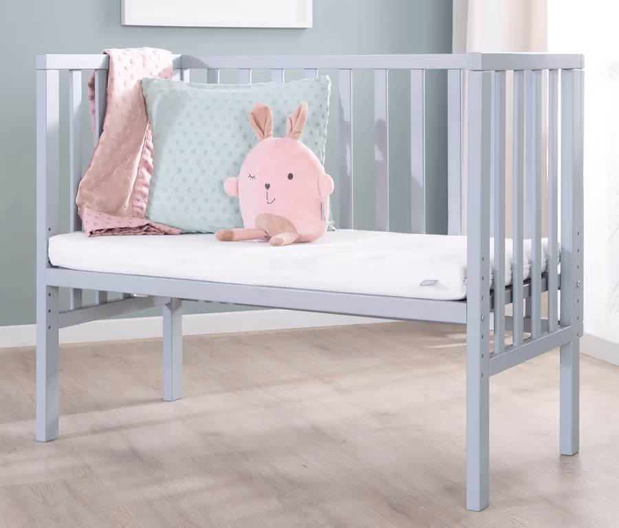 Ein hellblaues Kinderbett mit einem rosa Stoffhasen, einem Kissen und einer Decke. Im Bett liegt ein roba 2-in-1-Beistellbett »safe asleep®«, taupe.