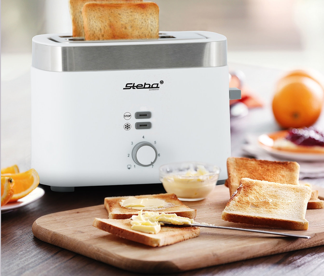 Zwei Toast im weißen Steba Toaster »TO 10 BIANCO«, weitere Toasts mit Butter auf Holzbrettchen.