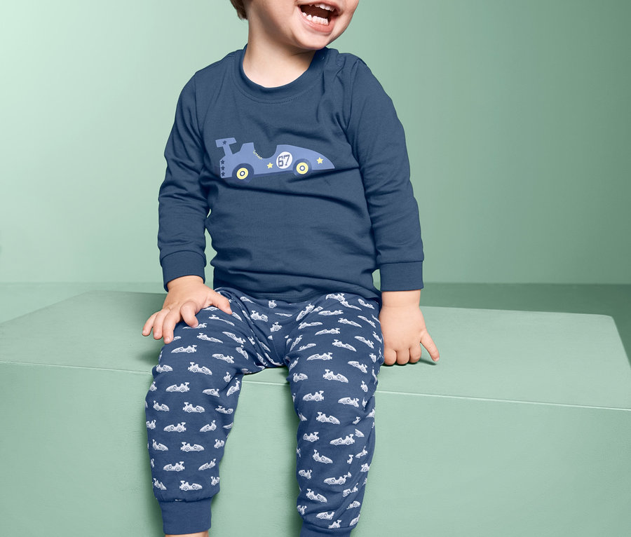 Lachender Junge sitzt auf einem grünen Block und trägt einen Pyjama.