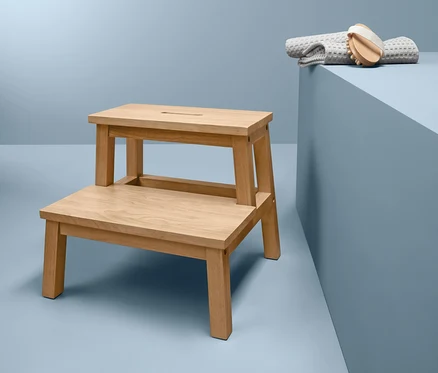 Ein Tritthocker aus Rubberwood steht neben einem grauen Handtuch und einer Bürste auf blauem Hintergrund.