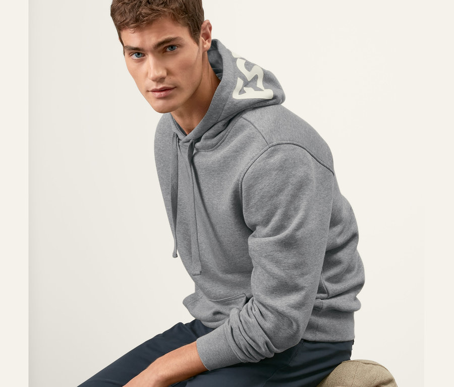 Mann sitzt auf Stuhl und trägt grauen Hoodie.