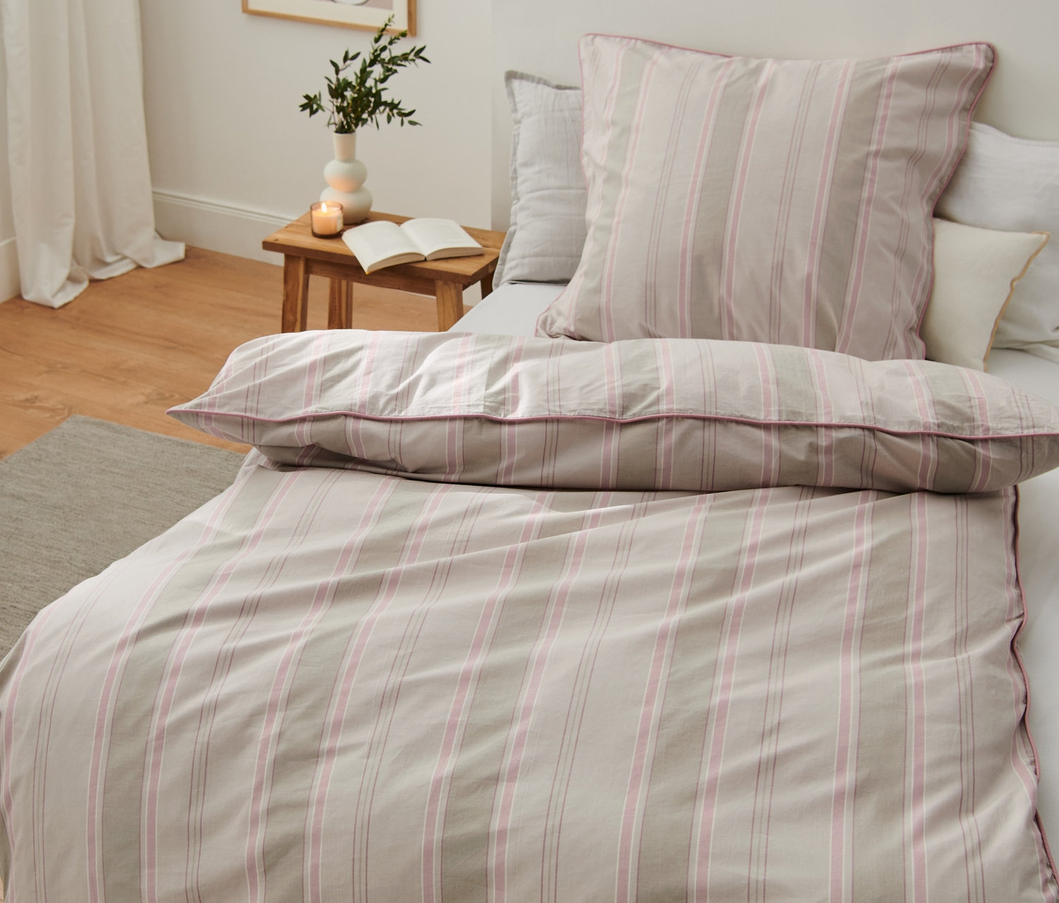 Schlafzimmer mit Bett mit Premium-Baumwoll-Bettwäsche in Normal- und Übergröße. Vase und Buch auf dem Nachttisch.