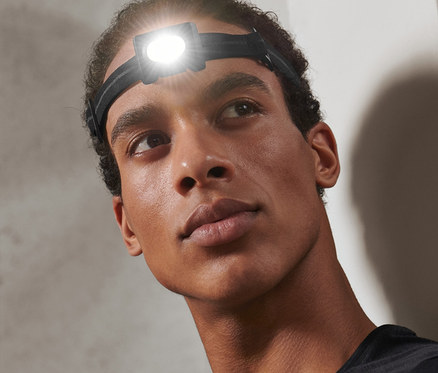 Mann mit Kompakter Stirnlampe auf dem Kopf schaut nach oben.