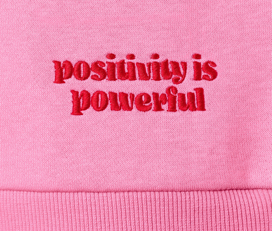 Detailaufnahme eines rosafarbenen Sweatshirts mit roter Stickerei "positivity is powerful".