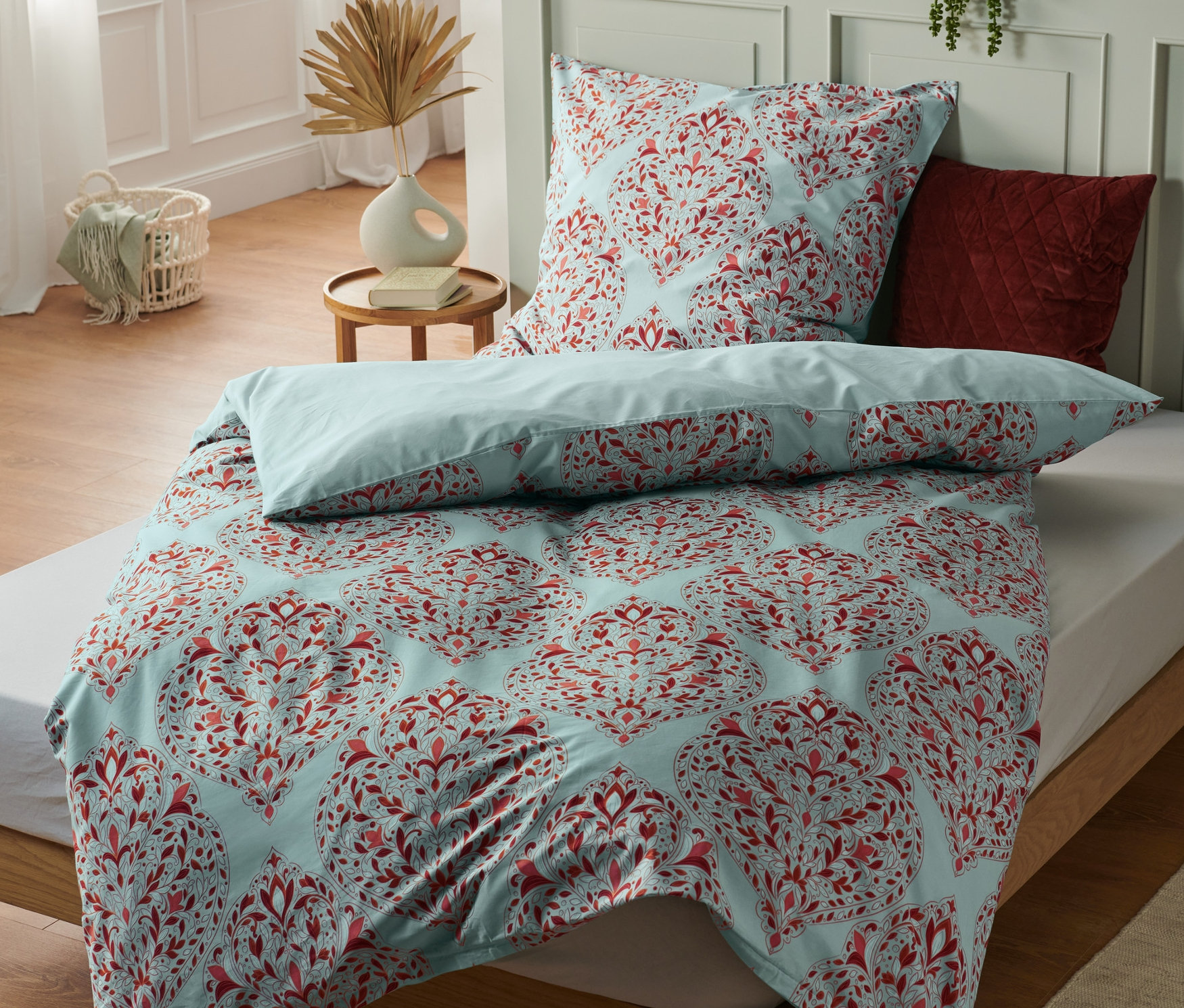 Ein Bett mit blauem Bettbezug mit rotem Blumenmuster. Auf dem Bett liegen drei Premium-Baumwoll-Bettwäsche in Normalgröße.